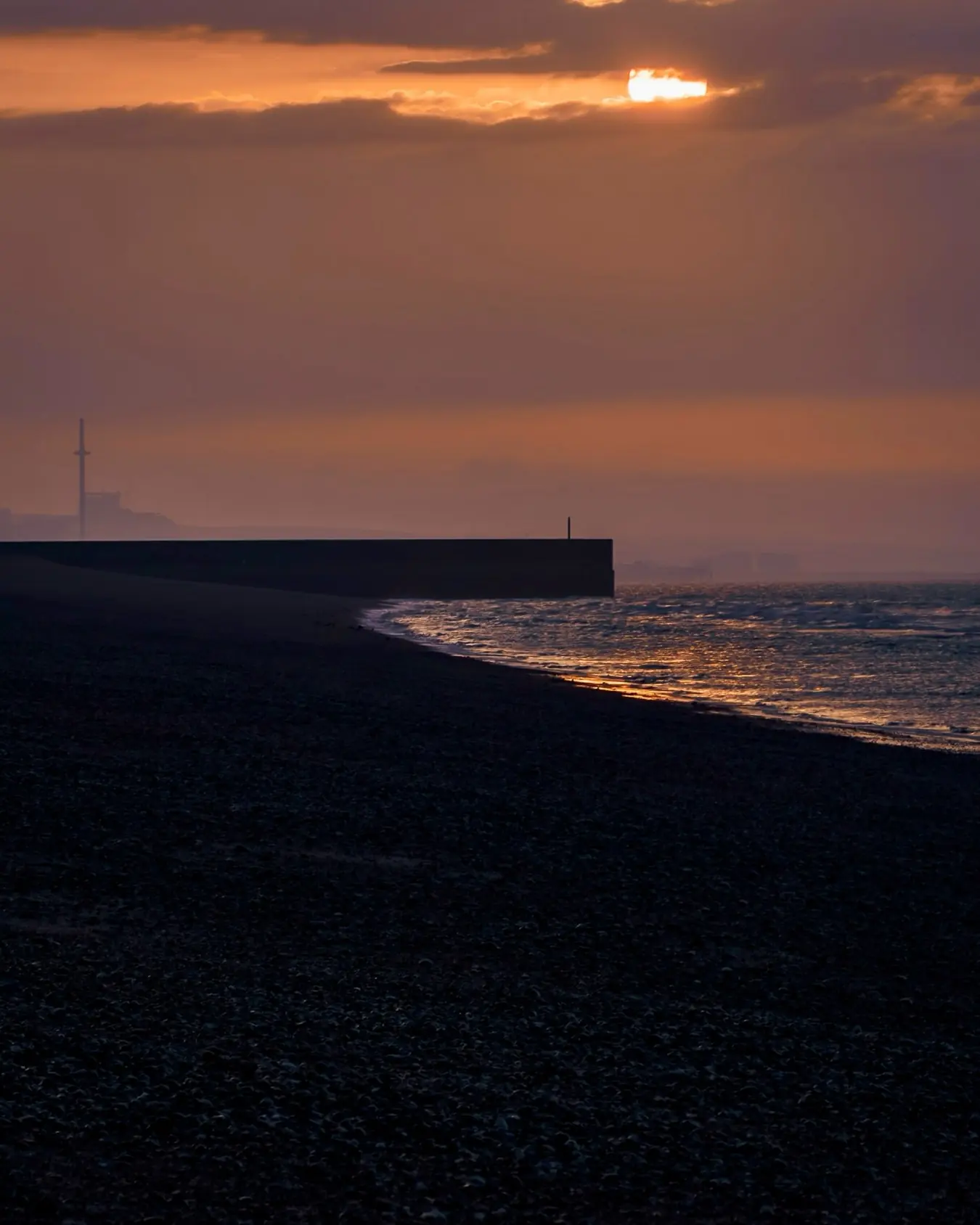 Low tide at first light on Shoreham beach, the harbour wall on the horizon