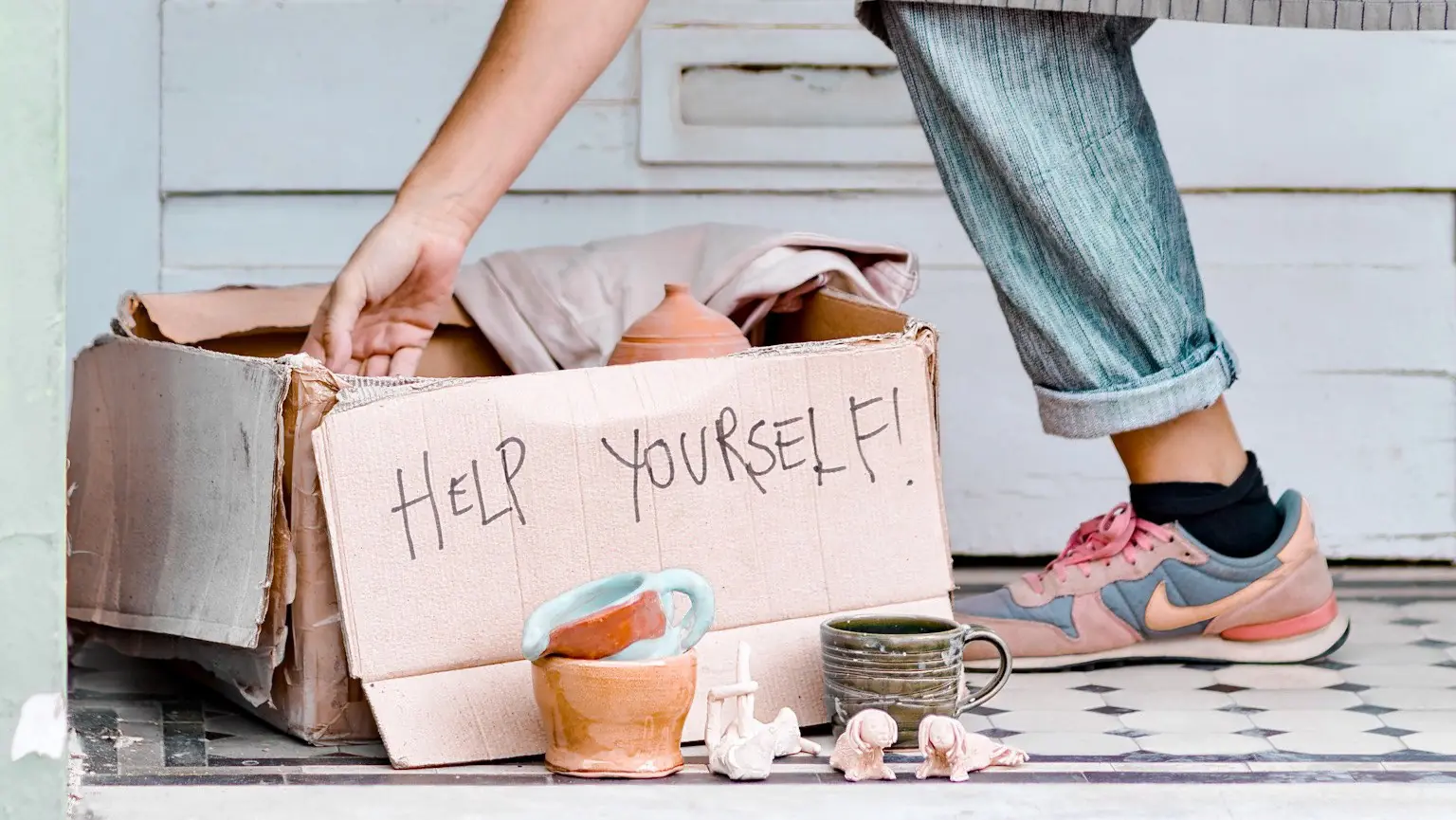 A potter in a teal T-shirt and grey apron smiles as she works clay at her bench.
